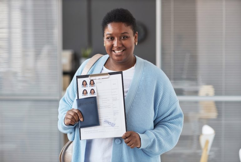 Young African American female applicant in casualwear looking at camera with smile while showing approved visa application form